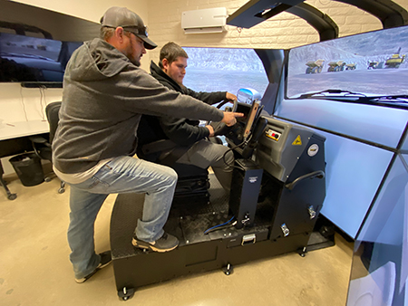 Matt McQuillan (standing) instructs Andre Gomez, Support Equipment Operator I, using a new simulator that virtually recreate the experience of driving a Ford F-250 pickup while autonomous haul trucks operate as they will in real life.